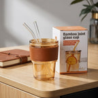 Bamboo joint glass cup with straws on a wooden surface next to its packaging.