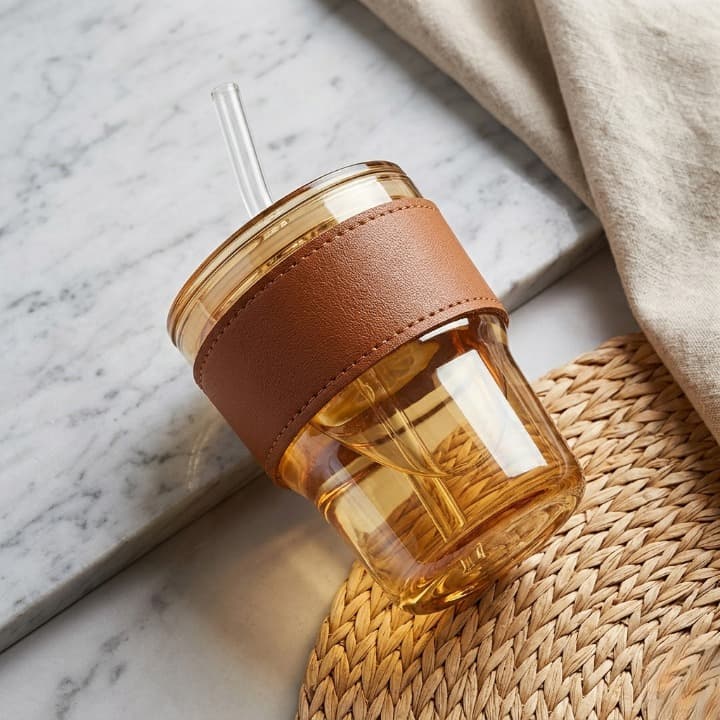 Glass tumbler with a brown leather sleeve and straw on a marble surface
