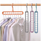 A set of four plastic hanger bars in peach, silver, lavender, and blue, shown hanging from a wooden rod alongside shirts on hangers.